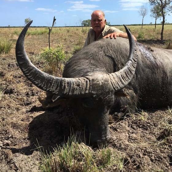 Hunter kneeling beside a water buffalo trophy in the field